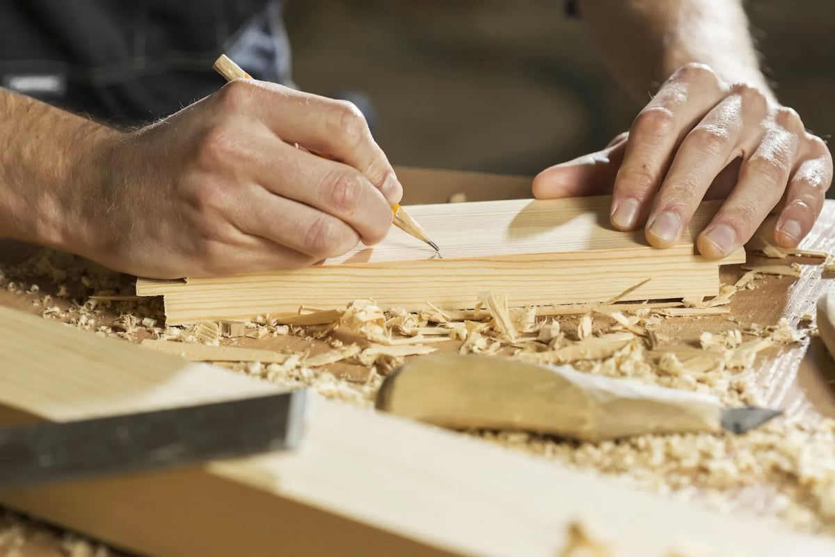 A hand marking a line with a pencil on a wooden board in a workshop