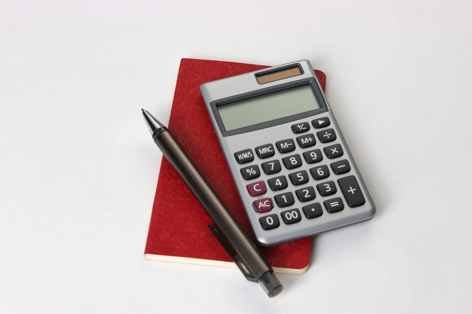A calculator and a pen on a red notebook