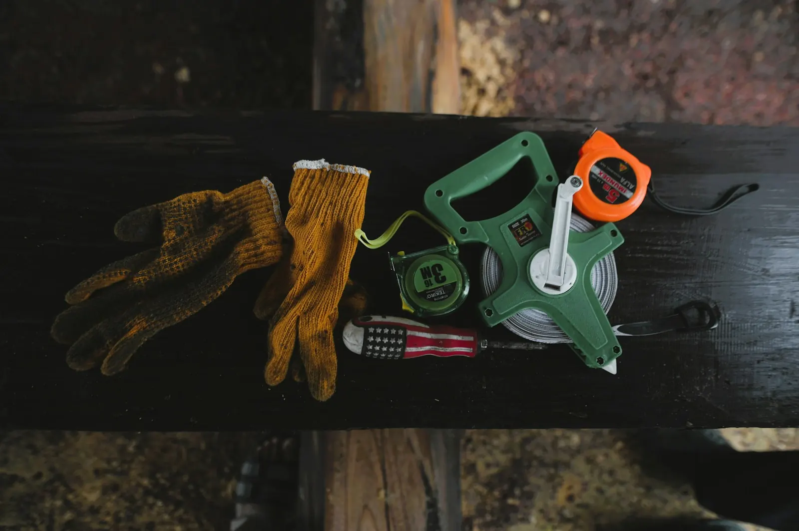 Work gloves, a screwdriver and two tape measures on a dark board